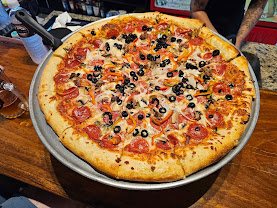 Supreme New York-style pizza with pepperoni, ham, black olives and veggies at The Pizza Shop in Jacó