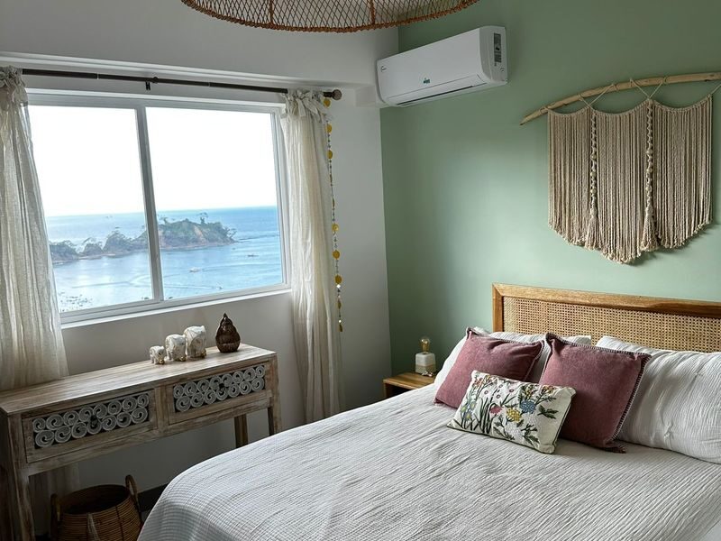 Master bedroom with direct ocean view window, split AC unit, and boho macramé decor — 2-bedroom apartment for sale at Playa Blanca near Jaco Beach, Costa Rica