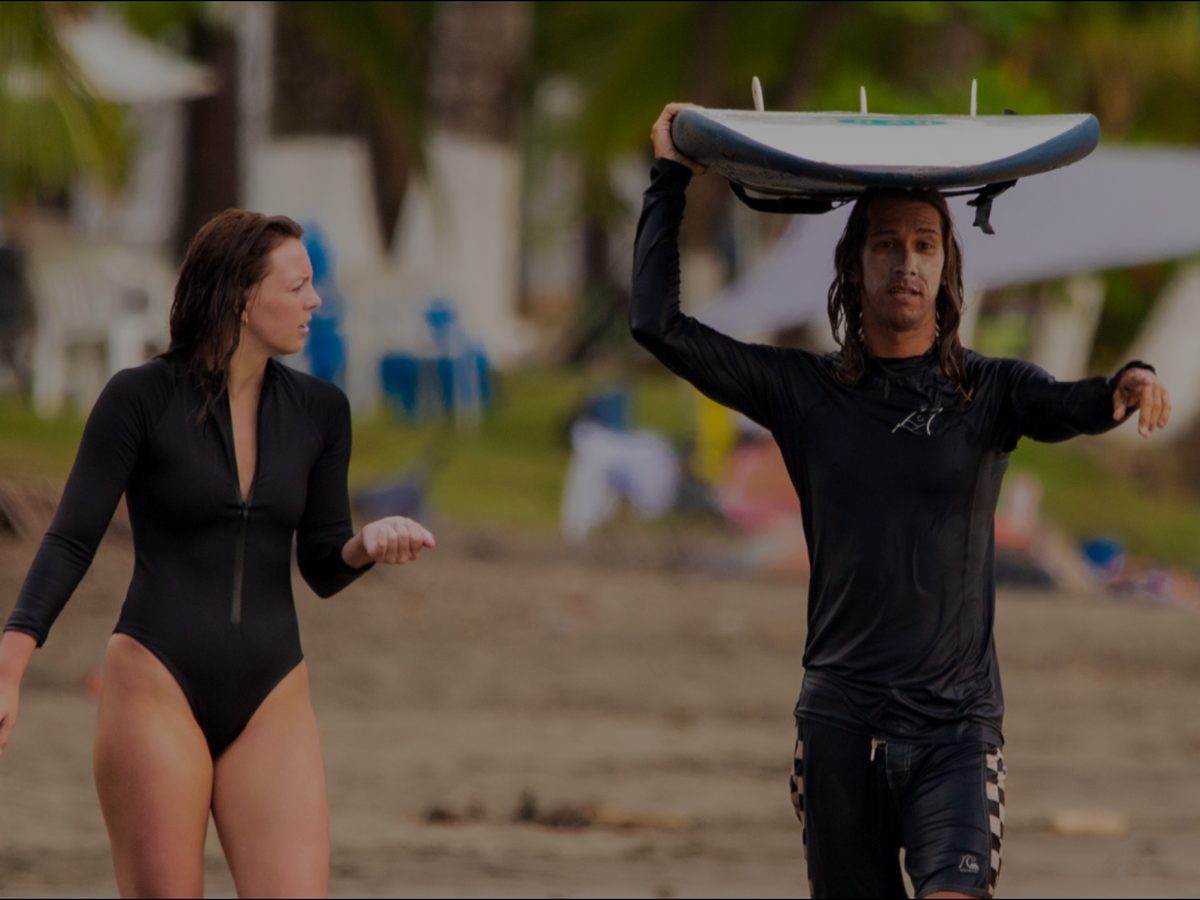 Surf student carrying her board on Jacó Beach